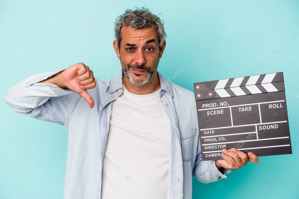 Middle age caucasian man holding a clapperboard isolated on blue background  showing a dislike gesture, thumbs down. Disagreement concept.