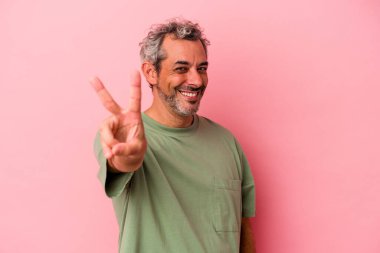 Orta yaşlı beyaz bir adam pembe arka planda izole edilmiş neşeli ve kaygısız parmaklarıyla barış sembolü gösteriyor..