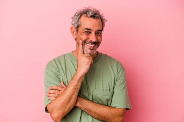 Orta yaşlı beyaz adam pembe arka planda izole edilmiş mutlu ve kendinden emin gülümsüyor, çenesine elleriyle dokunuyor..