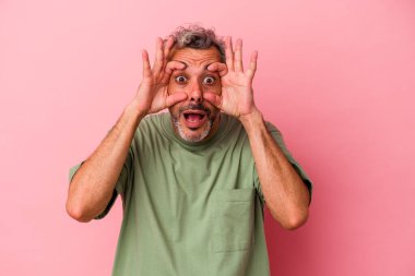 Pembe arka planda izole edilmiş orta yaşlı beyaz bir adam bir başarı fırsatı bulmak için gözlerini açık tutuyor..