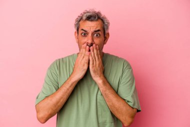 Orta yaşlı beyaz bir adam pembe arka planda izole edilmiş ağzı kapalı ve elleri endişeli görünüyor..