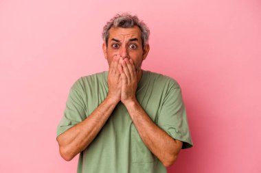 Orta yaşlı beyaz bir adam pembe arka planda izole edilmiş. Şok olmuş, ağzı ellerle kaplanmış, yeni bir şey keşfetmeye hevesli..