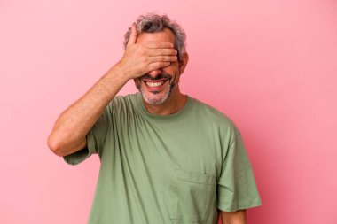 Pembe arka planda soyutlanmış orta yaşlı beyaz bir adam elleriyle gözlerini kapatıyor, büyük bir gülümsemeyle bir sürpriz bekliyor..