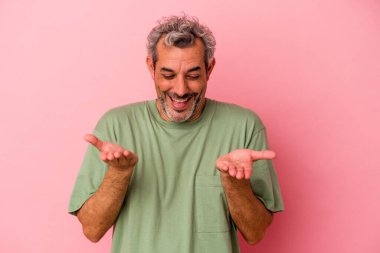 Orta yaşlı beyaz bir adam pembe arka planda izole edilmiş. Elinde avuç içi olan bir şeyle kameraya sunuyor..