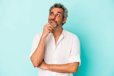 Mavi arka planda izole edilmiş orta yaşlı beyaz adam şüpheli ve şüpheci bir ifadeyle yana bakıyor..