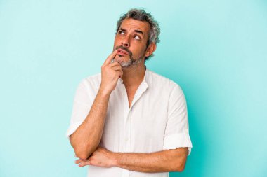 Mavi arka planda izole edilmiş orta yaşlı beyaz adam şüpheli ve şüpheci bir ifadeyle yana bakıyor..