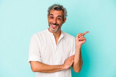 Mavi arka planda izole edilmiş orta yaşlı beyaz adam işaret parmağıyla işaret ederek gülümsüyor..