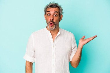 Mavi arka planda izole edilmiş orta yaşlı beyaz bir adam avuç içinin fotokopi alanından etkilenmiş..