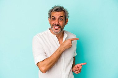 Mavi arka planda izole edilmiş orta yaşlı beyaz adam işaret parmağıyla fotokopi alanını işaret ederek şok oldu..