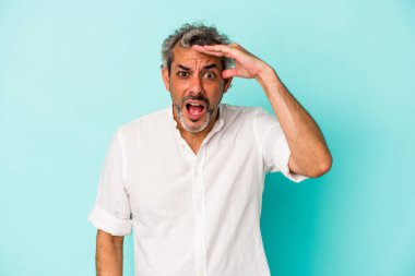 Mavi arka planda izole edilmiş orta yaşlı beyaz adam yüksek sesle bağırıyor, gözleri açık ve elleri gergin tutuyor..