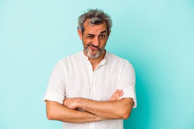 Orta yaşlı beyaz bir adam mavi arka planda izole edilmiş hoşnutsuzca kaşlarını çatmış, kollarını kavuşturmuş..