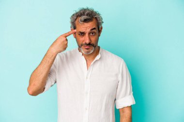 Mavi arka planda izole edilmiş orta yaşlı beyaz bir adam şakağı parmağıyla işaret ediyor, düşünüyor ve bir göreve odaklanıyor..