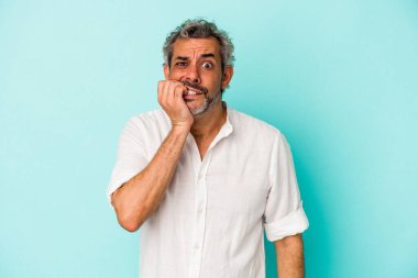 Mavi arka planda izole edilmiş, tırnak yiyen, gergin ve endişeli orta yaşlı bir beyaz adam..