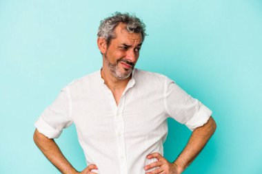 Mavi arka planda soyutlanmış orta yaşlı beyaz bir adam kafası karışmış, şüpheli ve kendinden emin değil..