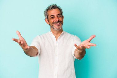 Mavi arka planda izole edilmiş orta yaşlı beyaz bir adam hoş bir ifade sergiliyor..