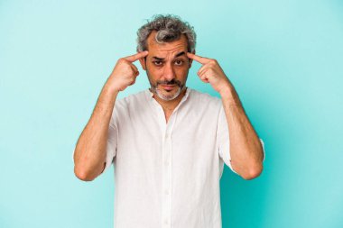 Mavi arka planda izole edilmiş orta yaşlı beyaz bir adam bir göreve odaklanmış, işaret parmaklarını işaret ediyor..