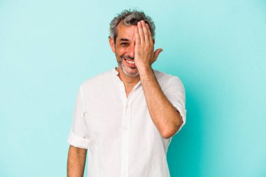 Mavi arka planda izole edilmiş orta yaşlı beyaz bir adam yüzünün yarısını palmiye ile örterek eğleniyor..