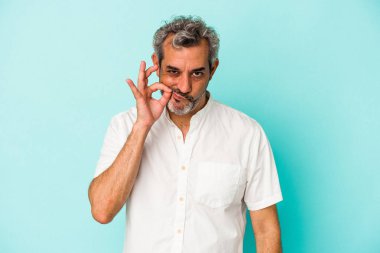 Orta yaşlı, beyaz bir adam mavi arka planda izole edilmiş ve parmakları dudaklarında bir sır saklıyor..