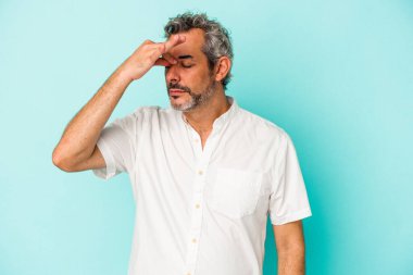 Orta yaşlı beyaz bir adam mavi arka planda izole edilmiş, başı ağrıyor, yüzüne dokunuyor..