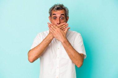 Orta yaşlı beyaz bir adam mavi arka planda izole edilmiş ağzı kapalı ve elleri endişeli görünüyor..