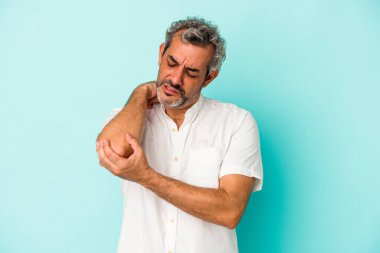 Orta yaşlı beyaz bir adam mavi arka planda izole edilmiş dirsek masajı yapıyor, kötü bir hareketin ardından acı çekiyor..