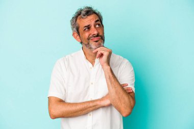 Orta yaşlı beyaz bir adam mavi arka planda izole edilmiş düşünüyor ve yukarı bakıyor, yansıtıyor, düşünüyor, bir fantezisi var..