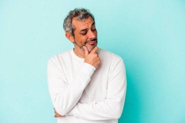 Mavi arka planda izole edilmiş orta yaşlı beyaz adam şüpheli ve şüpheci bir ifadeyle yana bakıyor..