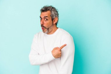 Mavi arka planda izole edilmiş orta yaşlı beyaz bir adam gülümsüyor ve boş alanda bir şeyler gösteriyor..