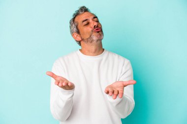 Orta yaşlı, beyaz bir adam mavi arka planda izole edilmiş dudaklarını katlıyor ve hava öpücüğü vermek için avuç içi tutuyor..