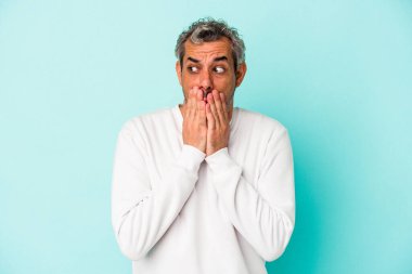 Orta yaşlı beyaz bir adam mavi arka planda izole edilmiş. Düşünceli bir şekilde bir fotokopi odasına bakıyor. Ağzını eliyle kapatıyor..