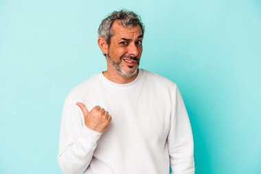 Mavi arka planda izole edilmiş orta yaşlı beyaz adam işaret parmağıyla fotokopi alanını işaret ederek şok oldu..