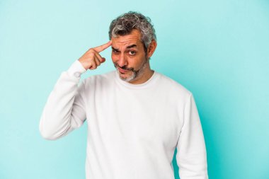 Mavi arka planda izole edilmiş orta yaşlı beyaz bir adam şakağı parmağıyla işaret ediyor, düşünüyor ve bir göreve odaklanıyor..