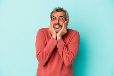 Orta yaşlı beyaz bir adam mavi arka planda izole edilmiş korkmuş ve korkmuş..