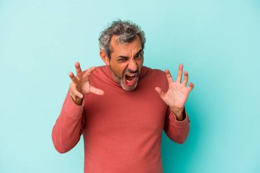 Mavi arka planda izole edilmiş orta yaşlı beyaz bir adam gergin elleriyle çığlık atıyor..