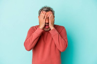 Mavi arka planda izole edilmiş orta yaşlı beyaz bir adam yüzünün yarısını palmiye ile örterek eğleniyor..