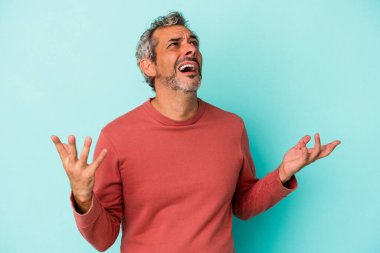 Mavi arka planda izole edilmiş orta yaşlı beyaz bir adam gökyüzüne haykırıyor, yukarı bakıyor, hayal kırıklığına uğramış..