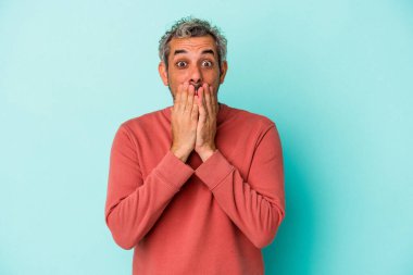 Mavi arka planda izole edilmiş orta yaşlı beyaz bir adam elleriyle ağzını kapatırken şok oldu..
