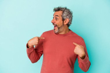 Mavi arka planda izole edilmiş orta yaşlı beyaz bir adam parmağını göstererek şaşırdı, geniş bir gülümsemeyle..