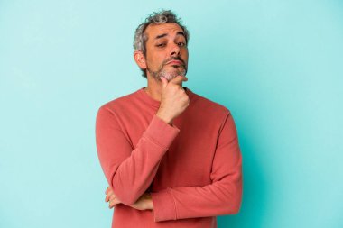 Orta yaşlı beyaz bir adam mavi arka planda izole edilmiş şüpheli, belirsiz, seni muayene ediyor..