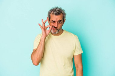 Orta yaşlı, beyaz bir adam mavi arka planda izole edilmiş ve parmakları dudaklarında bir sır saklıyor..