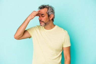 Orta yaşlı beyaz bir adam mavi arka planda izole edilmiş, başı ağrıyor, yüzüne dokunuyor..