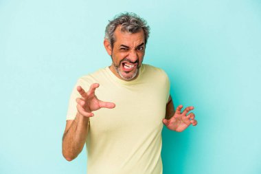 Mavi arka planda izole edilmiş orta yaşlı beyaz adam pençelerini kedi taklidi yaparken gösteriyor, agresif bir hareket..