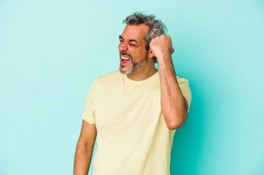 Mavi arka planda izole edilmiş orta yaşlı beyaz bir adam zaferi, tutkuyu ve coşkuyu kutluyor, mutlu bir ifade..