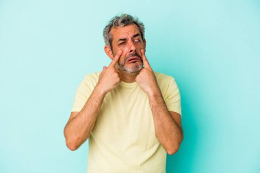 Orta yaşlı beyaz bir adam mavi arka planda izole edilmiş, ağlıyor, bir şeyden mutsuz, acı ve kafa karışıklığı konsepti..