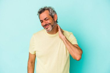 Orta yaşlı beyaz bir adam mavi arka planda izole edilmiş. Stres yüzünden boynu ağrıyor. Masaj yapıyor ve elle dokunuyor..