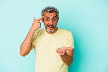 Orta yaşlı, beyaz bir adam mavi arka planda izole edilmiş ve elinde bir ürün var..