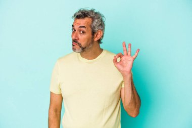 Orta yaşlı beyaz bir adam mavi arka planda izole edilmiş bir şekilde göz açıp kapayıncaya kadar iyi bir el hareketi yapıyor..