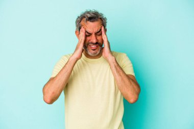 Orta yaşlı beyaz bir adam mavi arka planda izole edilmiş tapınaklara dokunuyor ve başı ağrıyor..