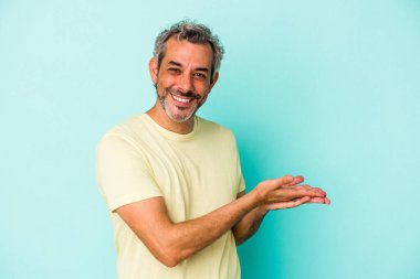 Mavi arka planda izole edilmiş orta yaşlı beyaz bir adam bir palmiye üzerinde bir kopya alanı tutuyor..