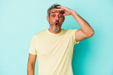 Orta yaşlı, beyaz bir adam, mavi arka planda izole edilmiş, uzaklara bakıyor, elini alnına koyuyor..